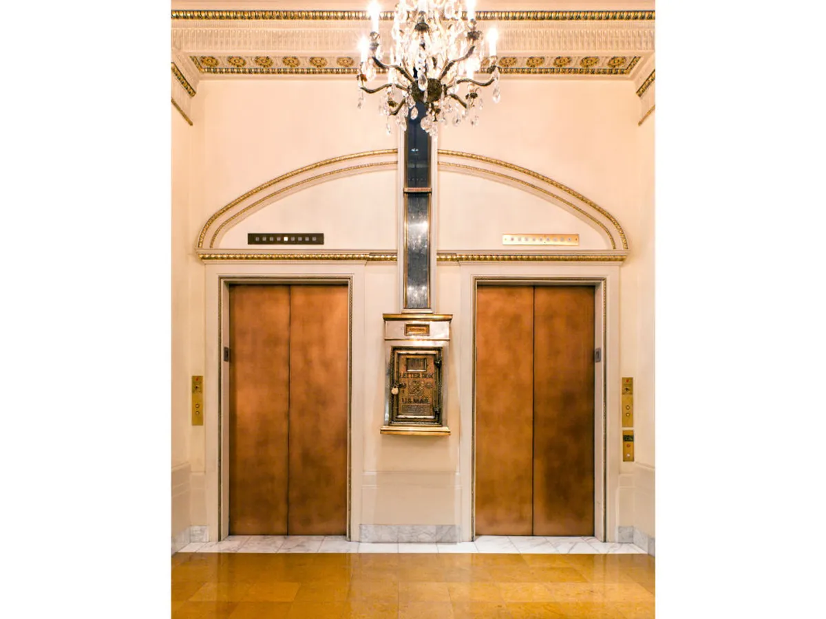 This image showcases the hotel's sophisticated lobby area, featuring elegant elevators, a graceful chandelier, and ornate historical detailing. The refined ambiance and visible entryway evoke a sense of memorable arrival and urban charm.