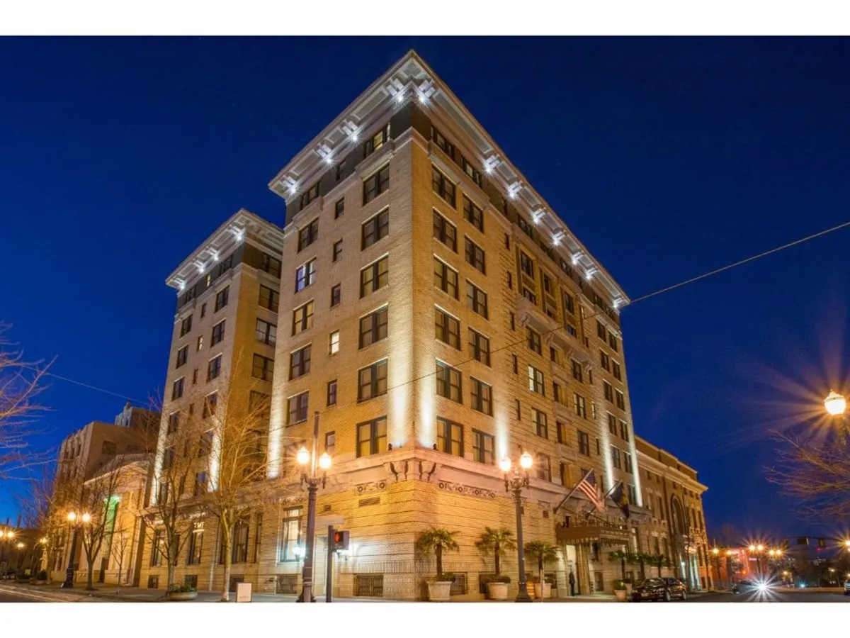 A nighttime exterior view of the building's illuminated façade, highlighting its sophisticated architectural details and vibrant city setting. Street lamps cast a warm glow, suggesting the excitement of Portland's nightlife and the hotel's proximity to local entertainment.