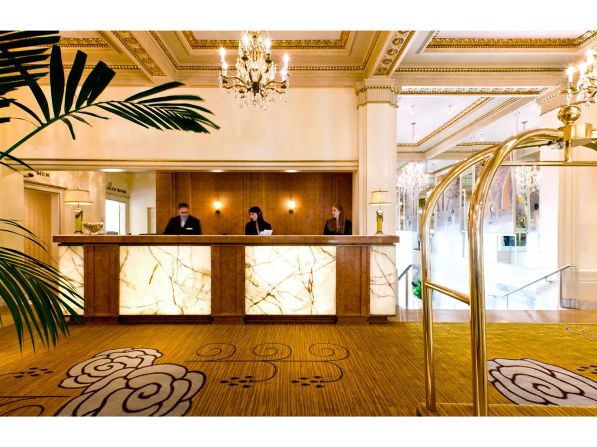 This image shows the hotel's reception area, featuring a luxurious chandelier overhead, a stylish reception desk, attentive staff members, and an ornate floral carpet design. The setting radiates an inviting and upscale atmosphere, setting the tone for the personalized service offered throughout the hotel.