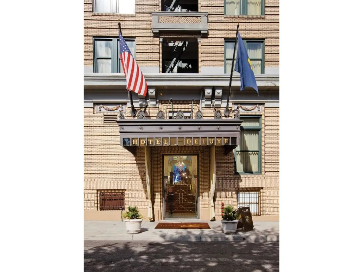 A welcoming view of the hotel’s main entrance, complete with prominent signage, fluttering flags, and a sophisticated exterior. The scene suggests arrival, anticipation, and the transition from plush hotel comfort to lively urban exploration.
